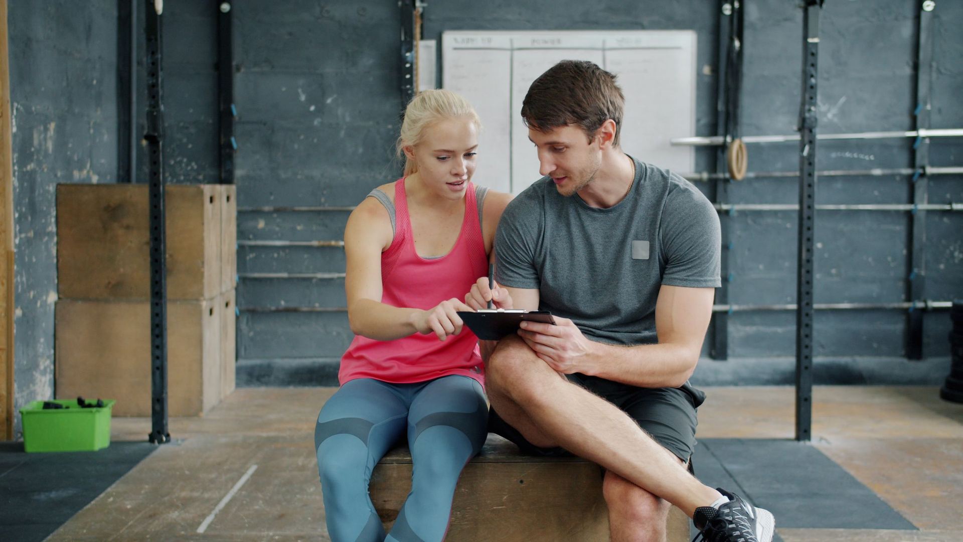 A coach and a client going over a plan on a tablet in a gym